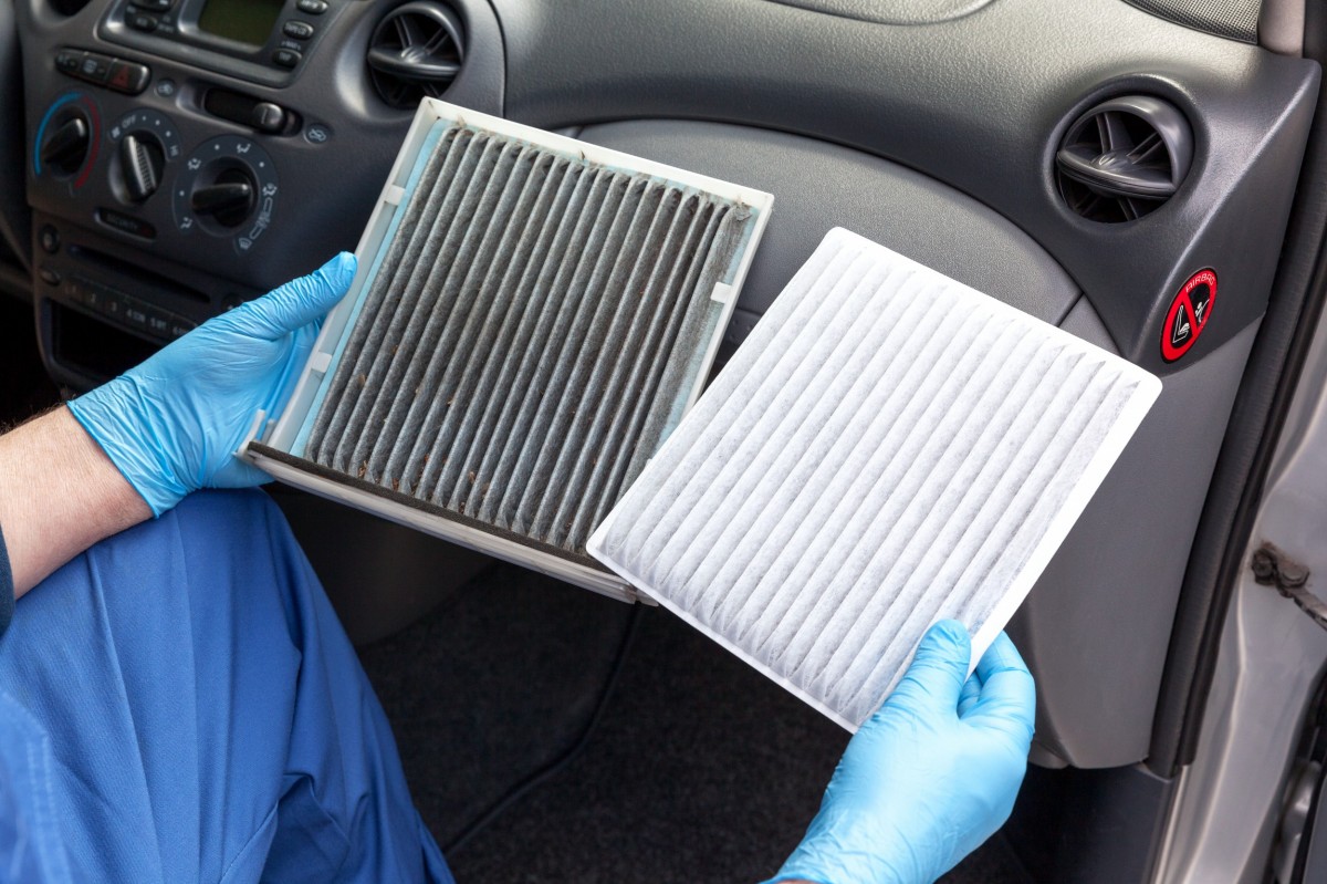 technician holding a clean and dirty air filter comparison in the front seat of a car